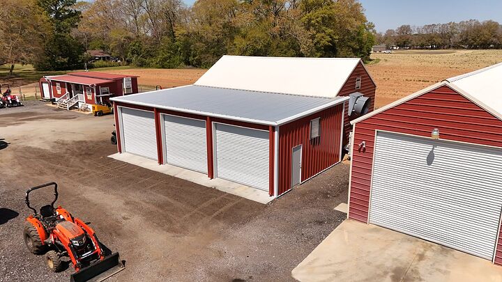 Aerial view of a red metal shop with three roll-up doors and a gray roof
