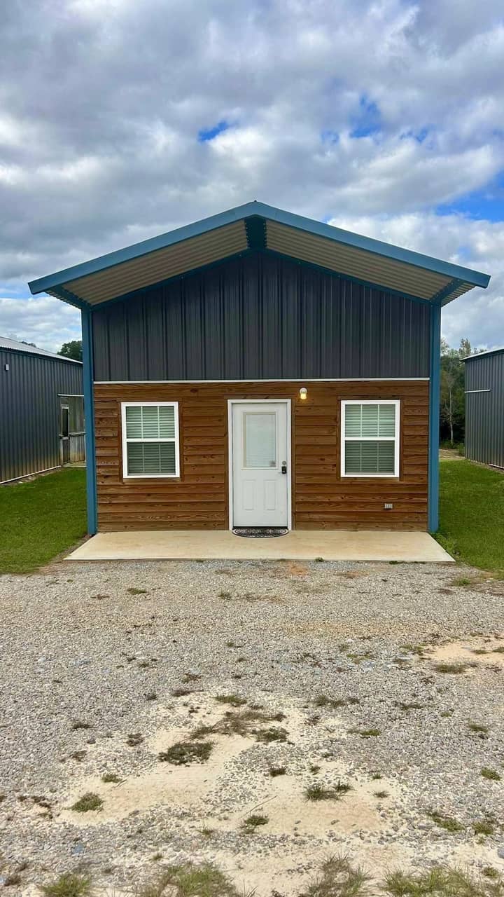 Metal cabin with green walls and wood accent on a gravel drive