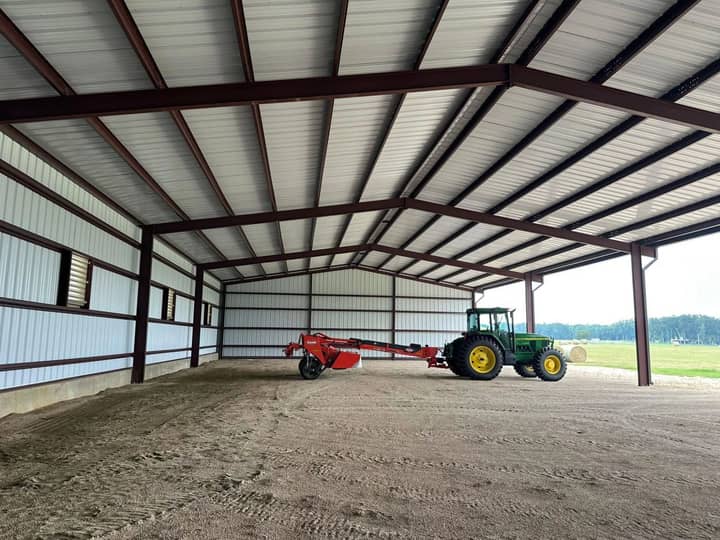 Inside a clear-span steel equipment shelter with a tractor and hay rake