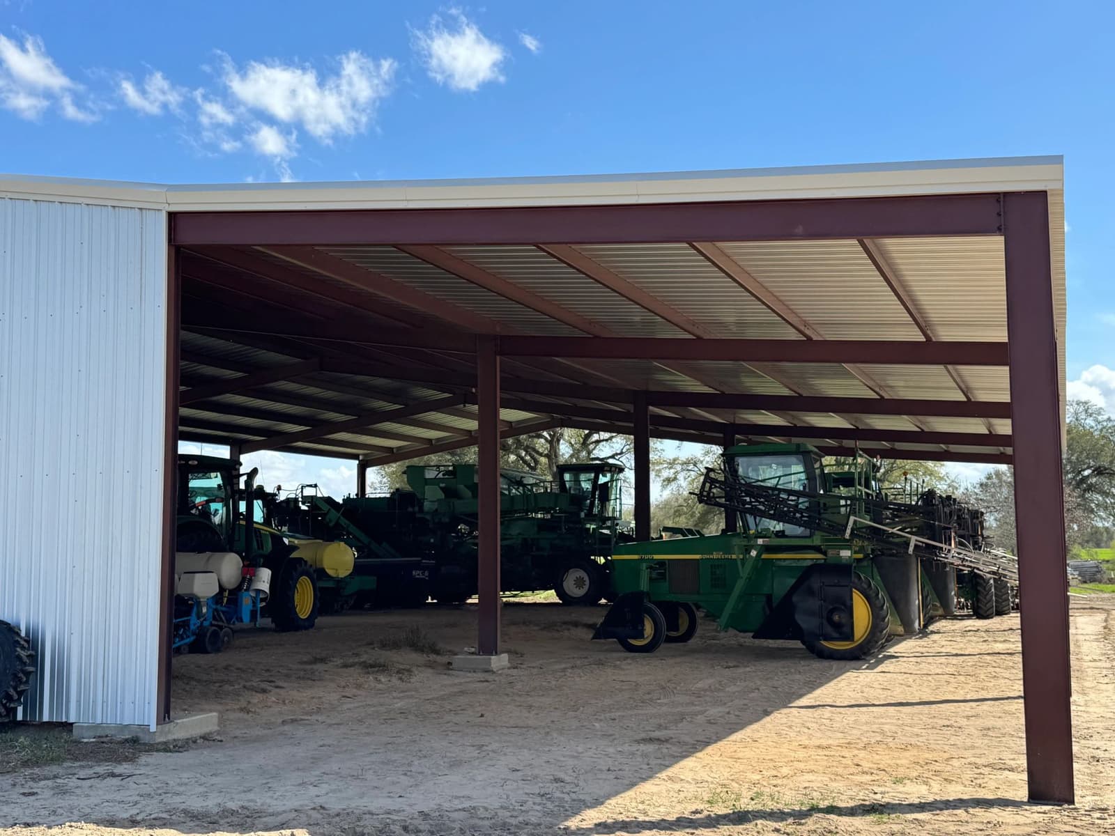 Red steel frame equipment shed sheltering sprayers and tractors