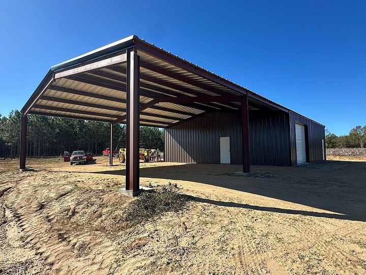 Gray metal building with a wide red iron lean-to over new graded ground