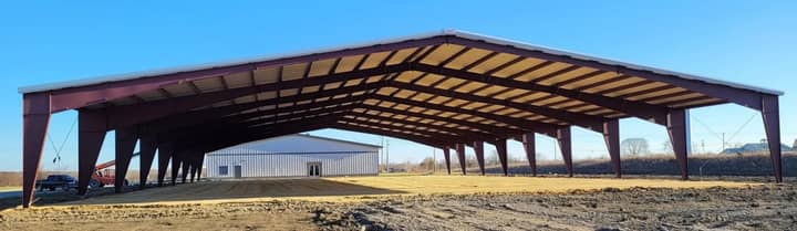 Long open-sided metal pavilion with red rigid steel frames under a blue sky