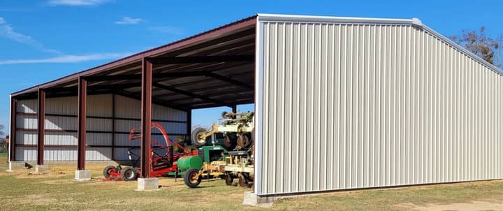 Tan metal building with an open lean-to sheltering farm equipment