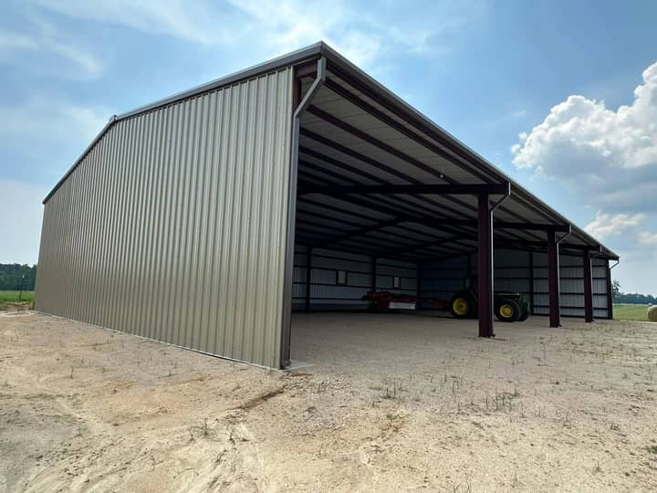 Tan metal building with an open side and red frame bays