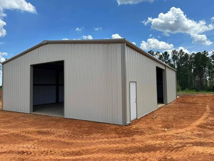 Tan metal shop with open bay door on fresh red dirt