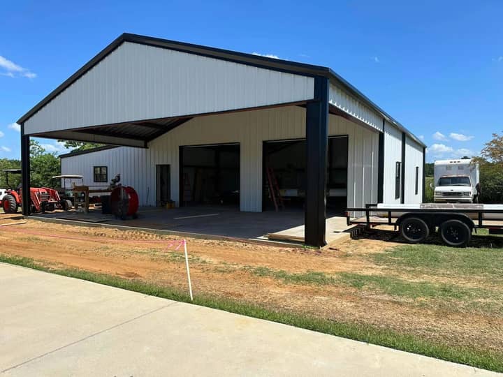 White metal shop with black trim and a tall drive-through lean-to